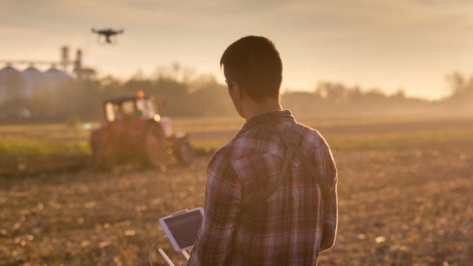 A man is standing in a field with a drone in the background.