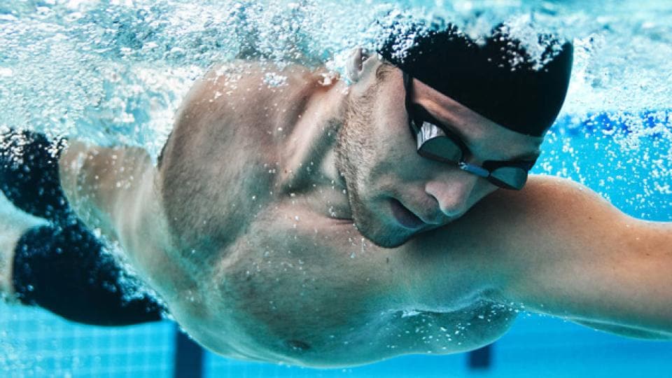 A man swimming in a pool with goggles on.